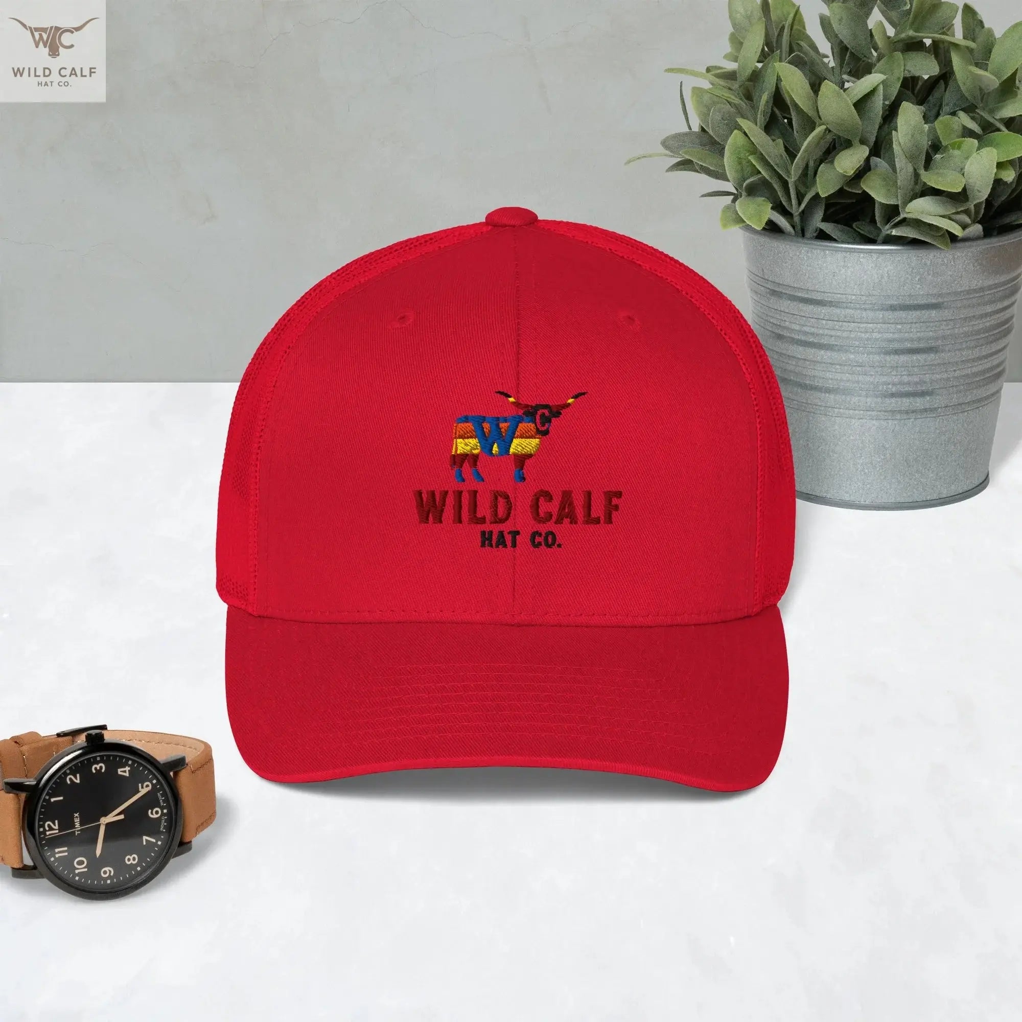 Red retro trucker hat with embroidered western calf logo, displayed on a marble surface.