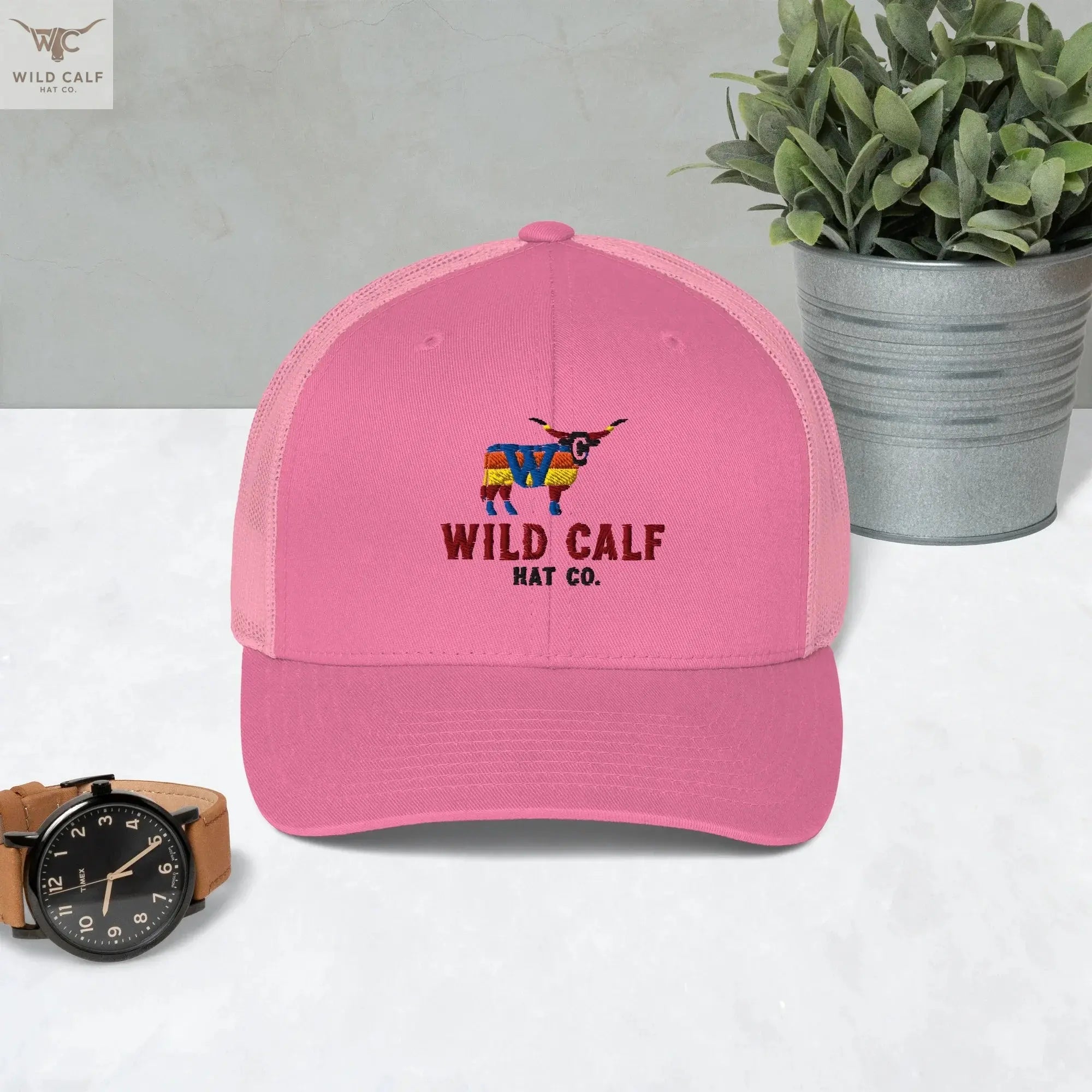 Pink retro western trucker hat with embroidered colorful longhorn logo, on marble surface