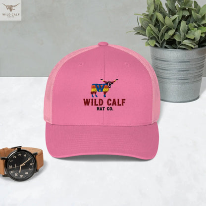 Pink retro western trucker hat with embroidered colorful longhorn logo, on marble surface